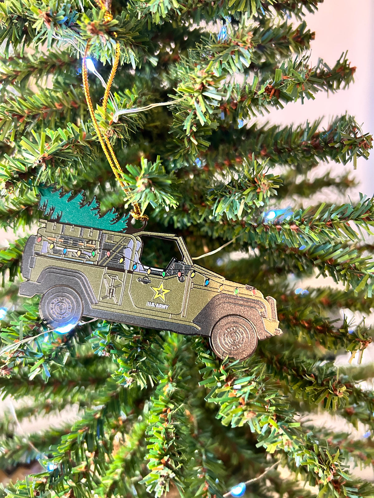 Olive-drab U.S. Army Jeep Christmas ornament carrying a Christmas tree, with string lights and Army star on the door